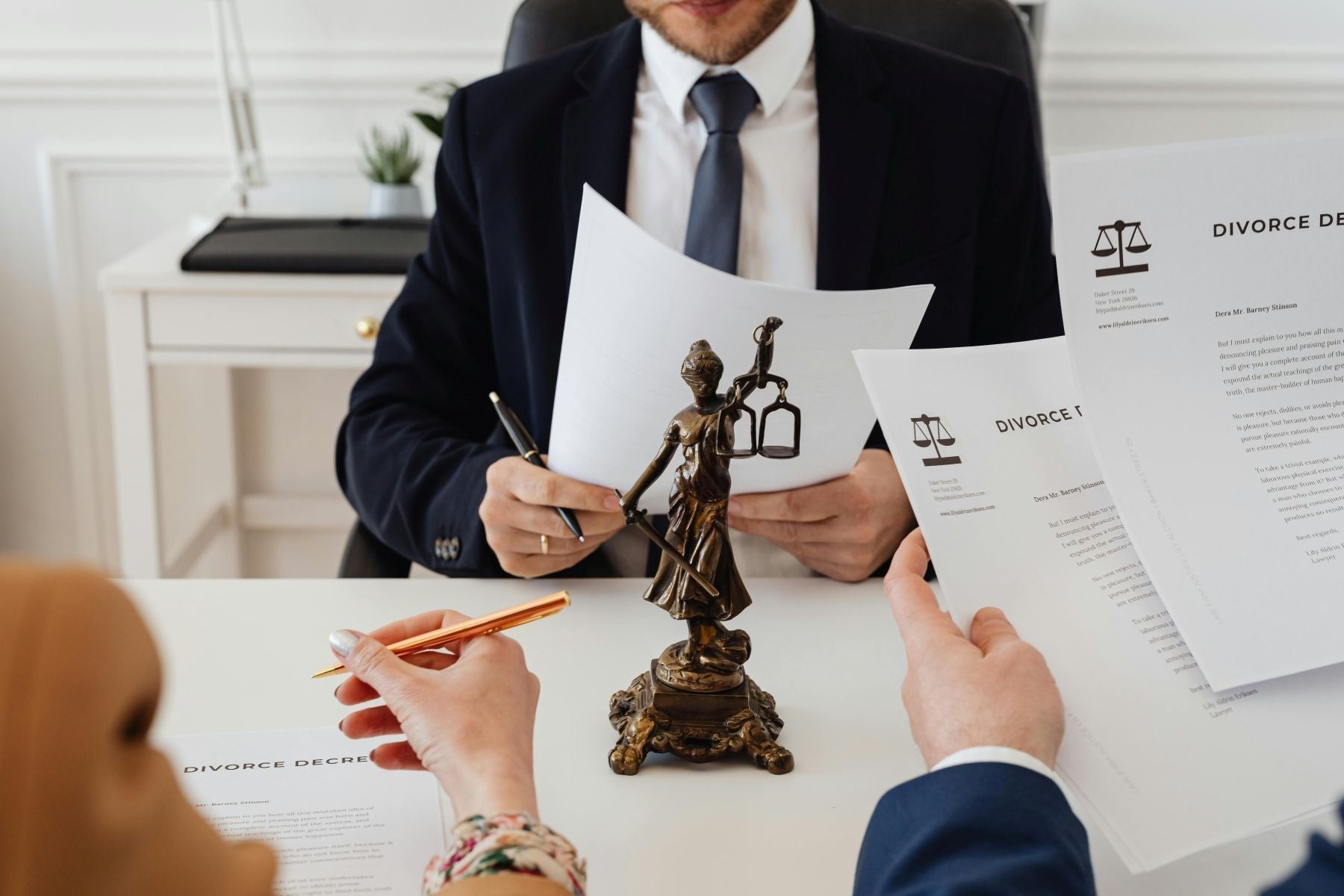 Two people and a suited professional review divorce documents around a small Lady Justice statue, emphasizing the need to update estate plans during significant life events such as divorce.