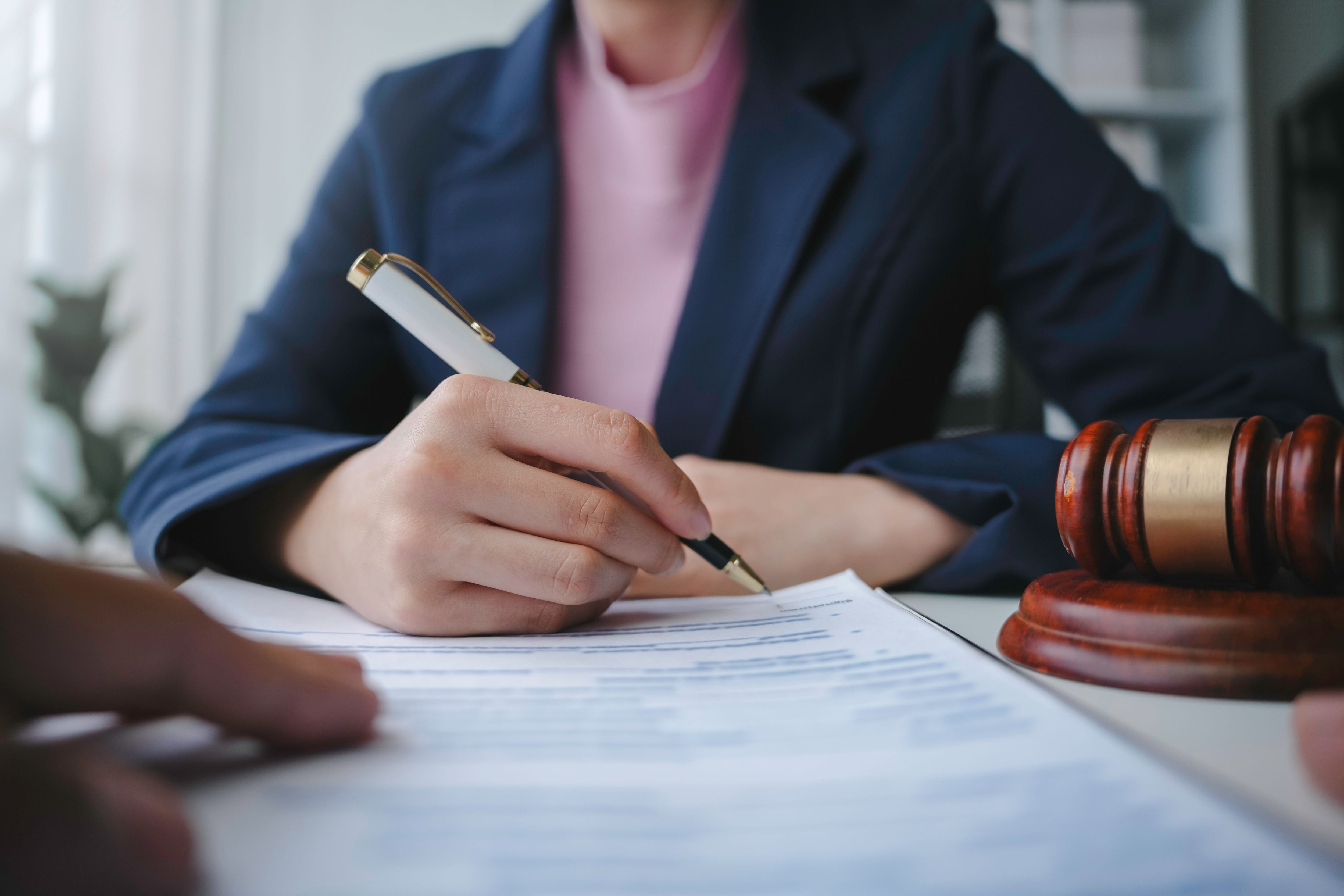 Close-up of a legal professional reviewing and signing estate planning documents, including wills, trusts, and power of attorney forms, with a gavel in view—representing the importance of organizing legal paperwork for future planning.