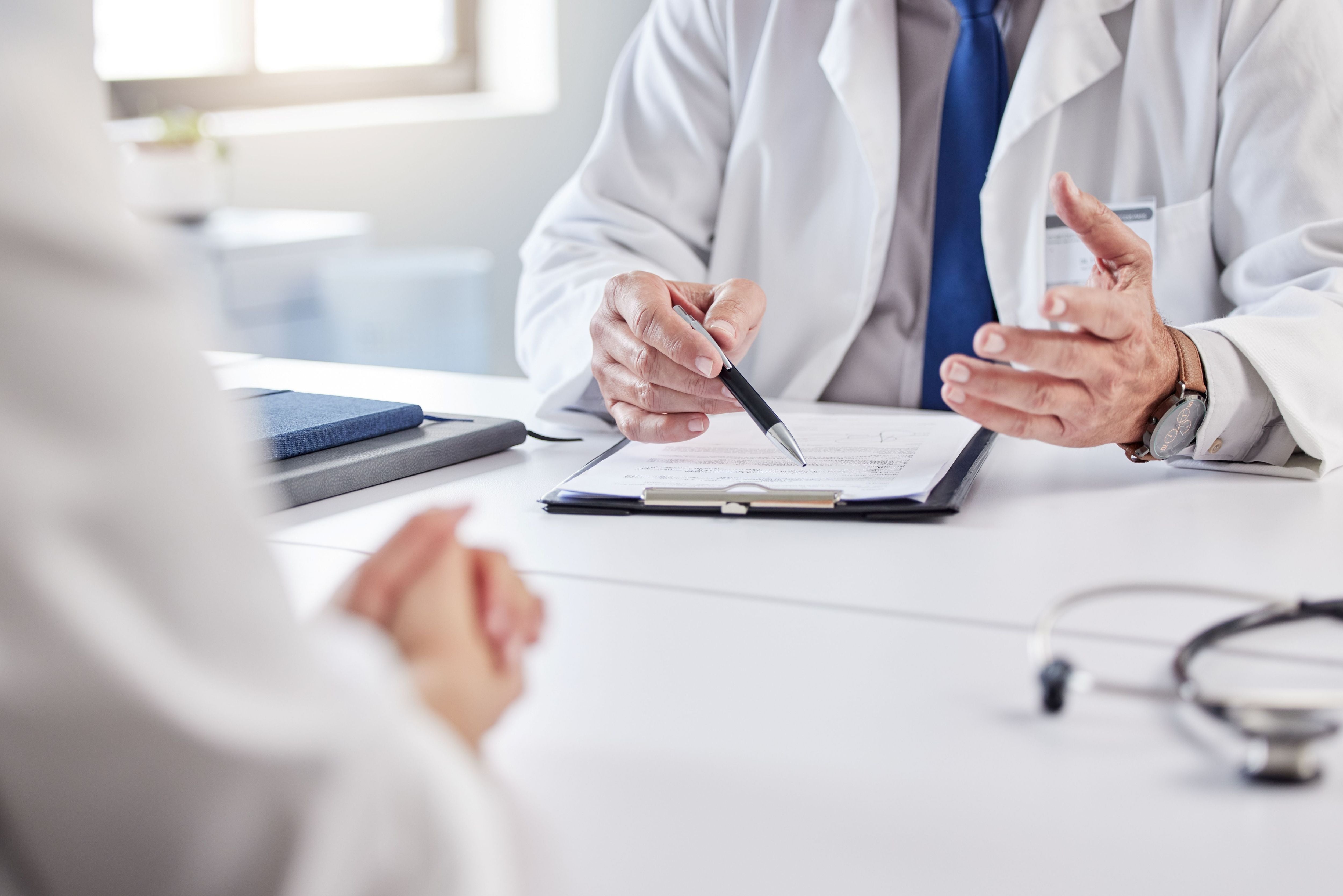 A doctor discussing medical paperwork with a patient across a desk, symbolizing the importance of organizing health insurance documents with tools like the OWL Planner.
